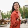 Young latina woman smiling and walking in city with braids Carefree young woman with long braids smiles while walking through a city square during summer